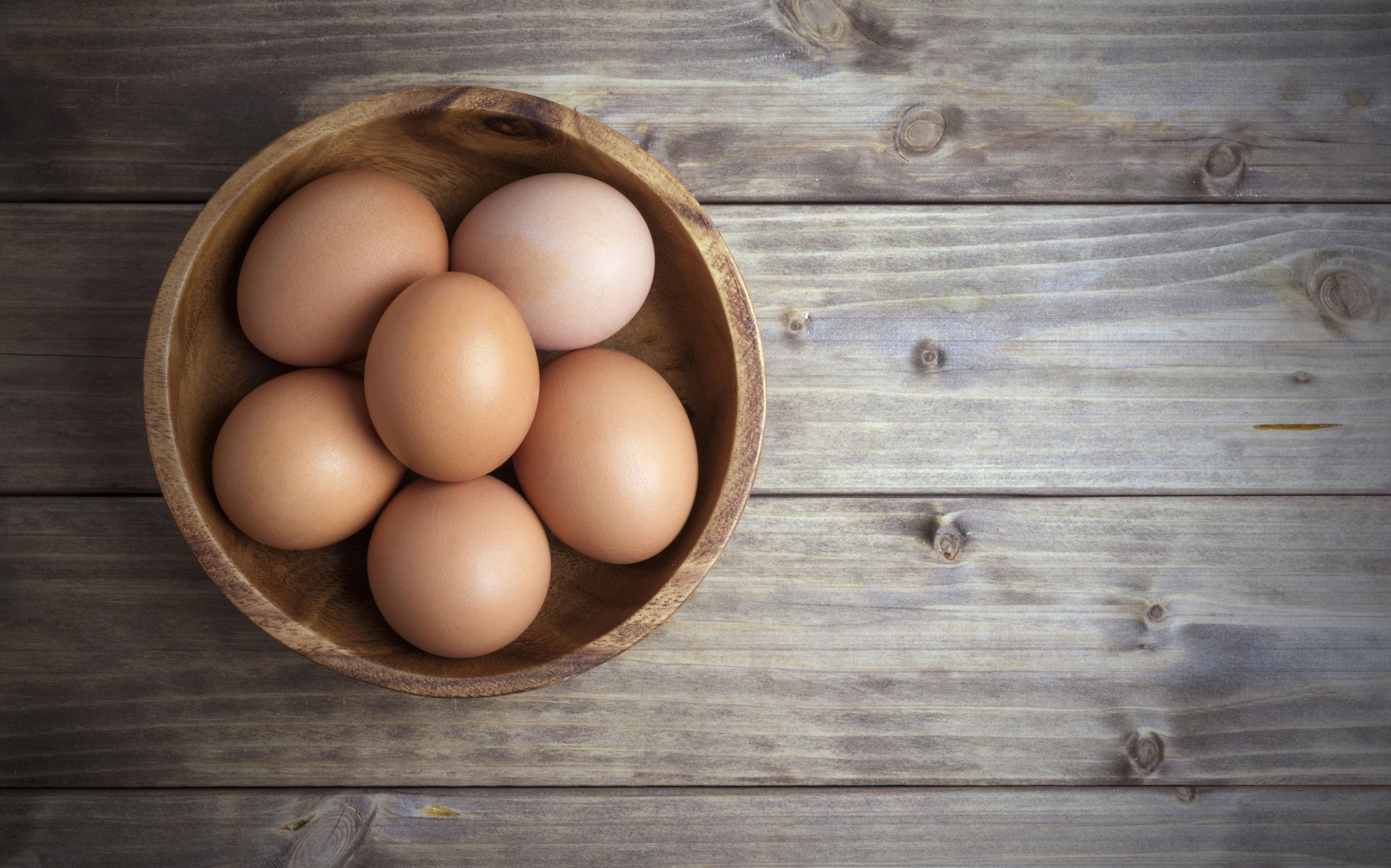 Bowl of brown eggs sitting on a wooden table.