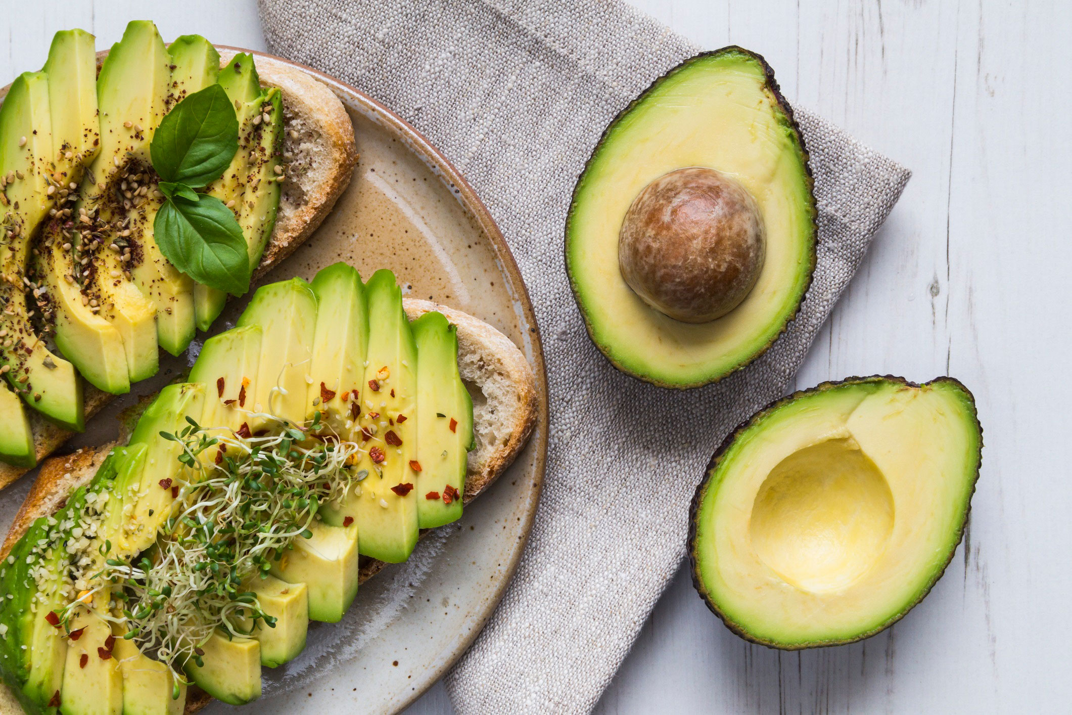 Plate of sliced avocado with seasoning next to two halves of an avocado.