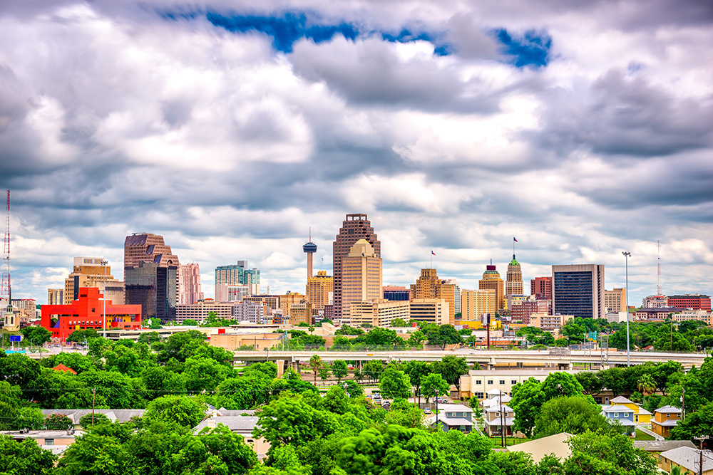 The view of vibrant trees leading up to downtown San Antonio under a cloud sky.