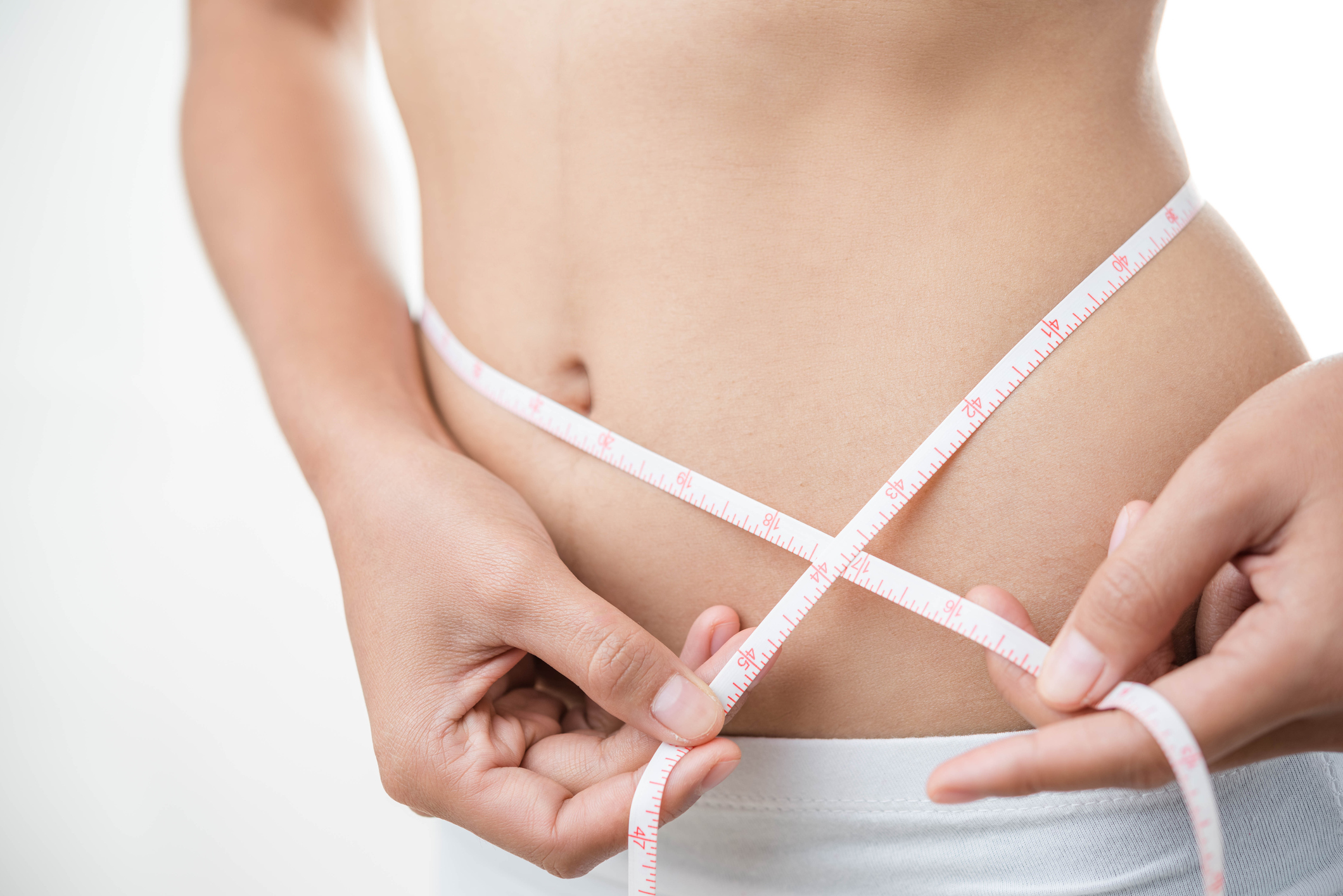 Woman abdomen with measuring tape over grey background.