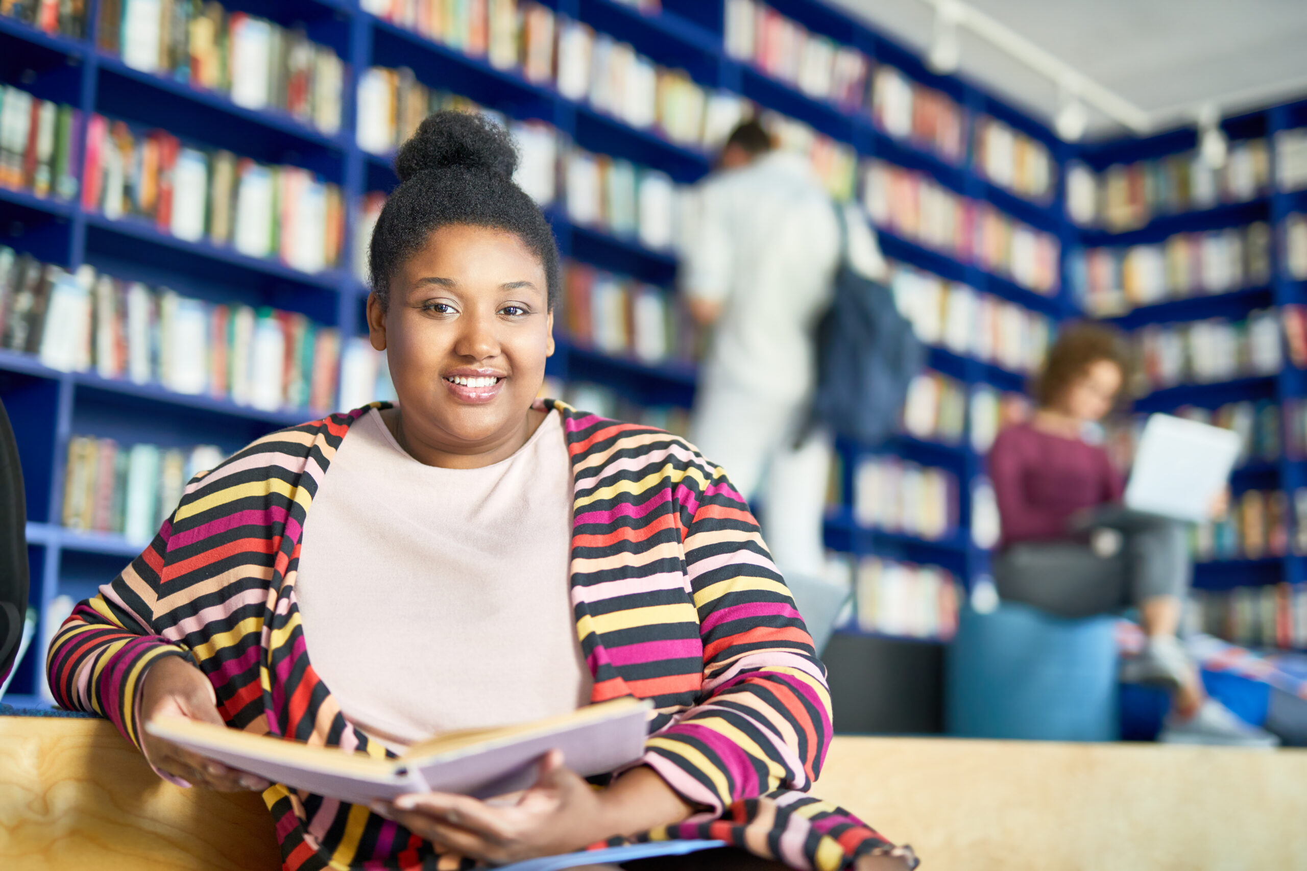 Overweight woman in a library, smiling at camera while holding book.