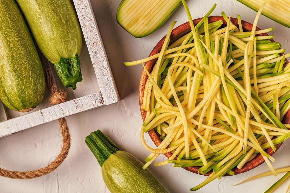 Whole zucchini placed around bowl of thin strips of zucchini.